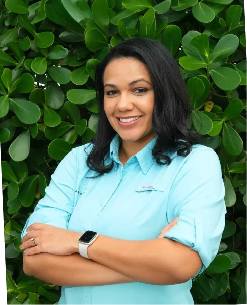 Abagail Lyon, Mint Eco Car Wash team member, smiling in a teal branded shirt in front of green foliage