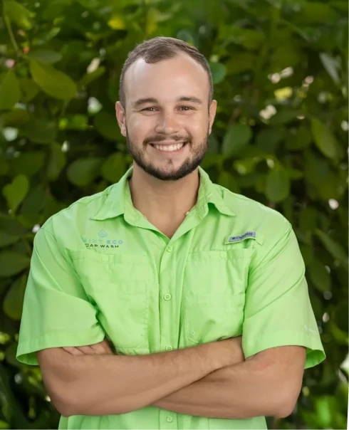 Bobby Cano, Mint Eco Car Wash team member, smiling in a light green branded shirt in front of green foliage