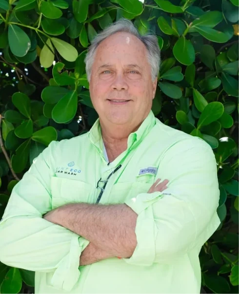 Duncan Davis, Mint Eco Car Wash team member, smiling in a light green branded shirt in front of green foliage