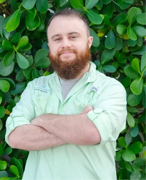 Kevin Harris, Mint Eco Car Wash team member, smiling in a light green branded shirt in front of green foliage
