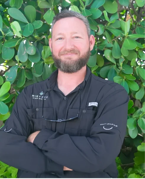 Michael Burford, Mint Eco Car Wash team member, smiling in a black long-sleeve branded shirt in front of green foliage