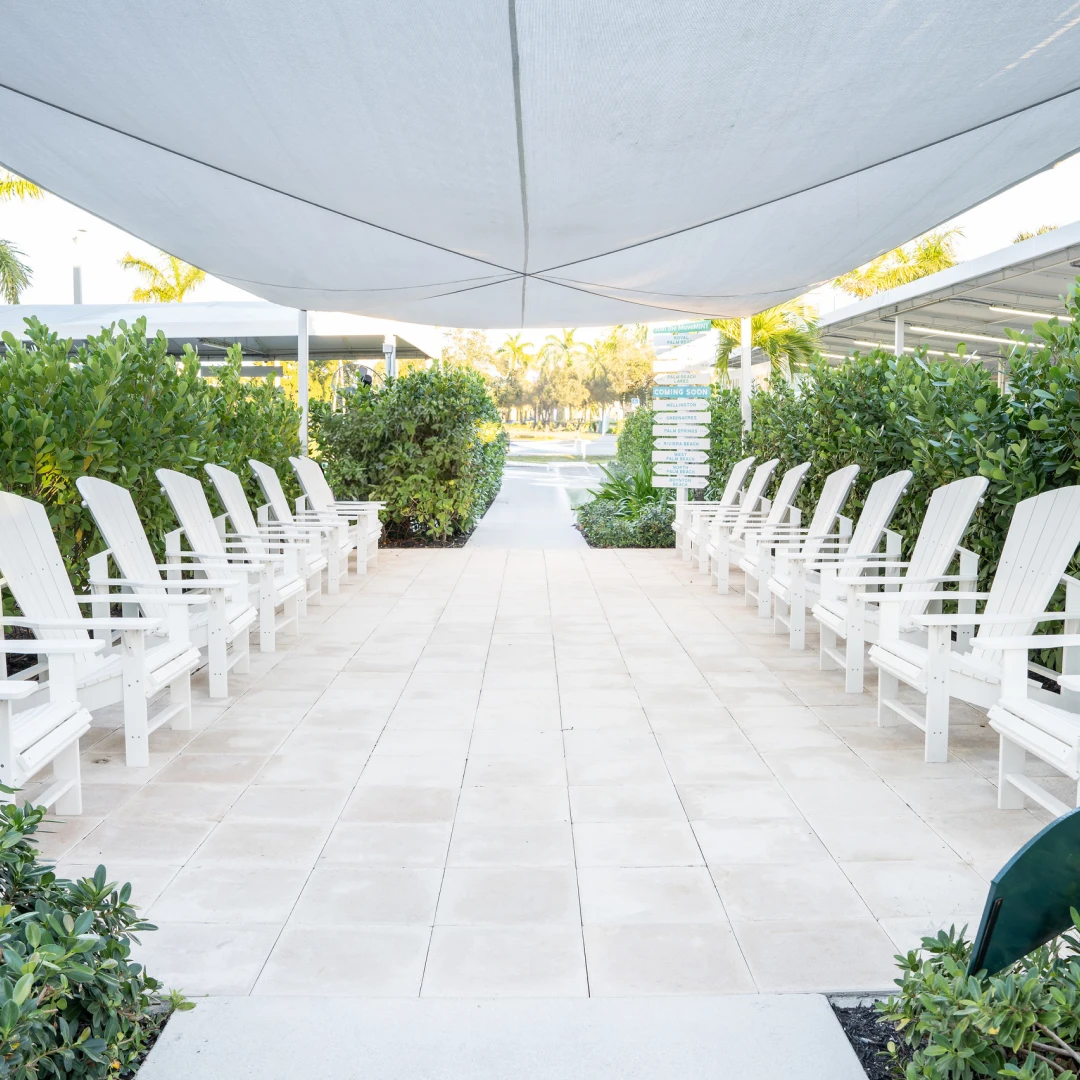 Row of white lounge chairs under a shade sail at a Mint Eco Car Wash location