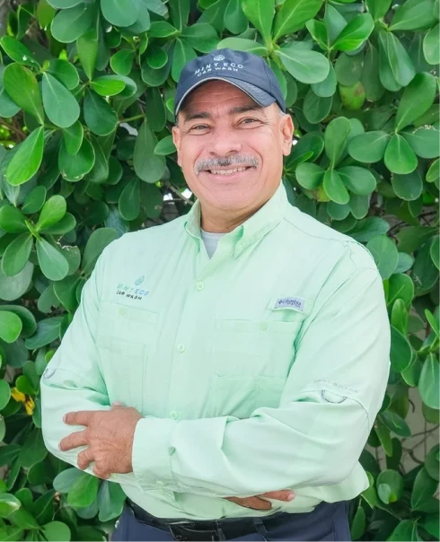 Tony Morales, Mint Eco Car Wash team member, wearing a branded cap and light green shirt, smiling in front of green foliage