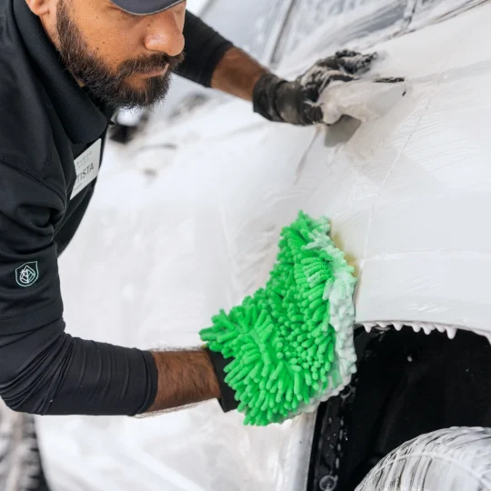 Employee hand-washing a car with a green microfiber wash mitt