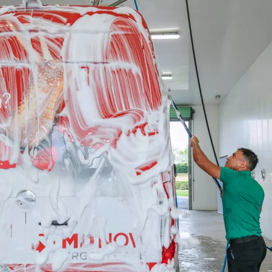 Employee hand-washing a van covered in soap suds