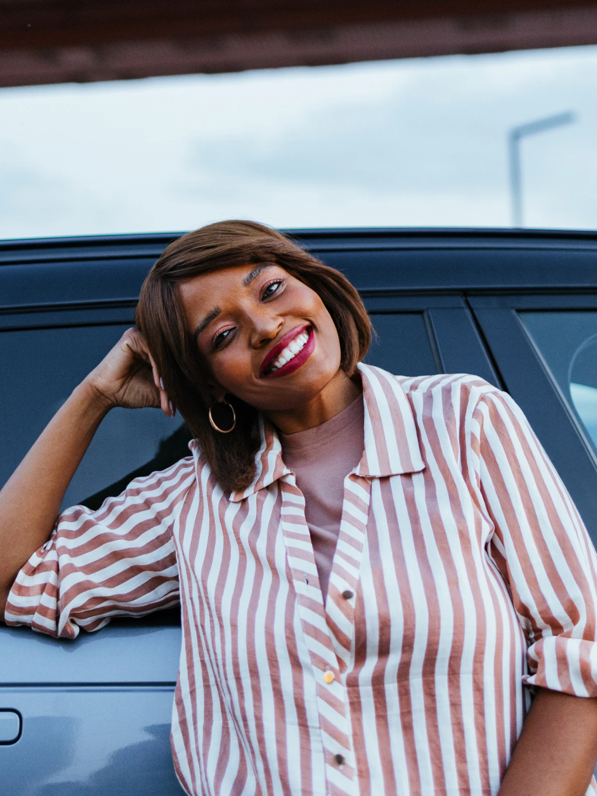 Woman in a striped shirt leaning against a car