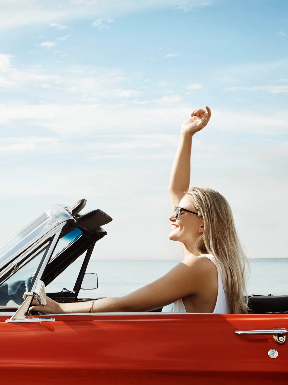 Woman smiling and leaning out the window of a blue Jeep near the beach