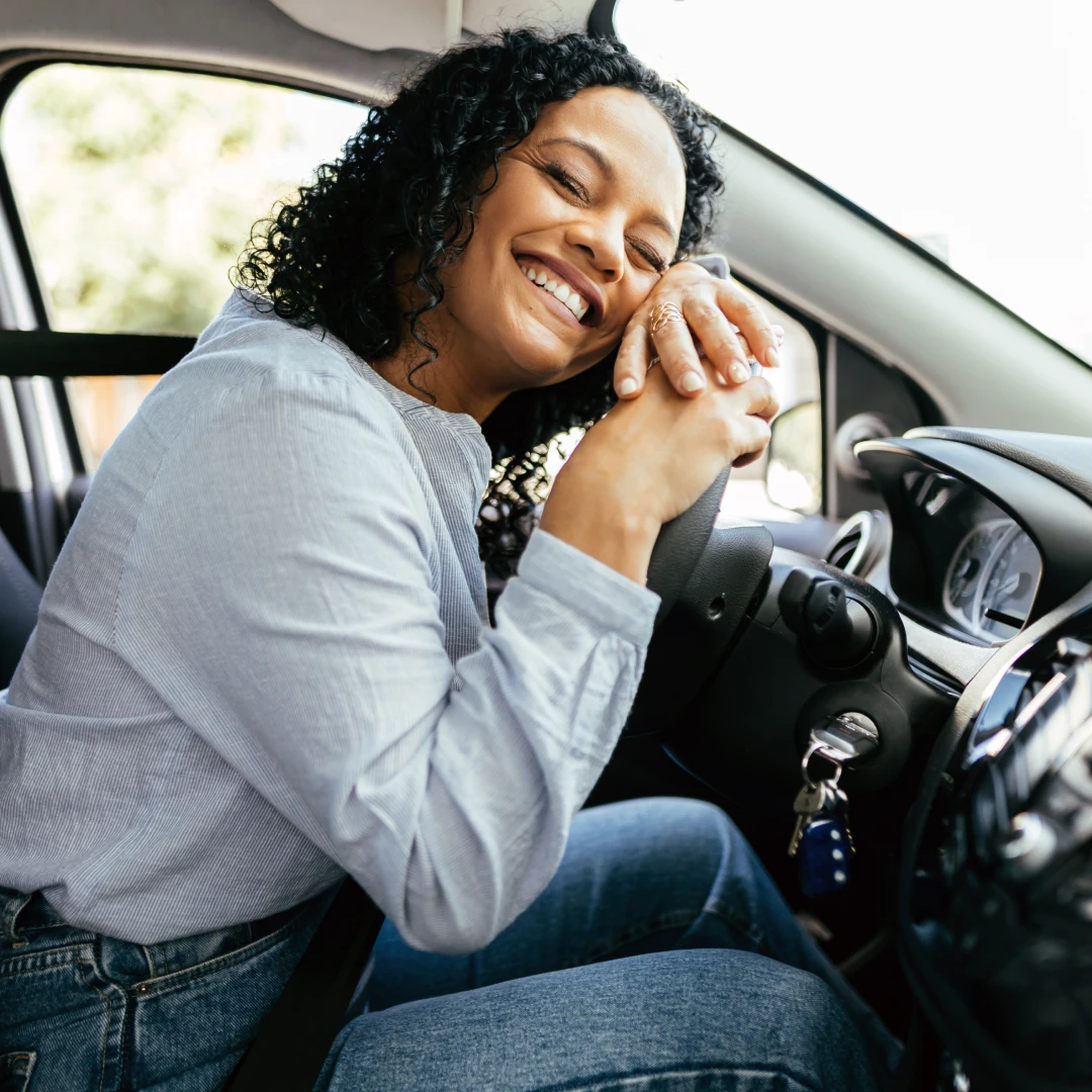 Woman laughing with her head resting on her hands on the steering wheel