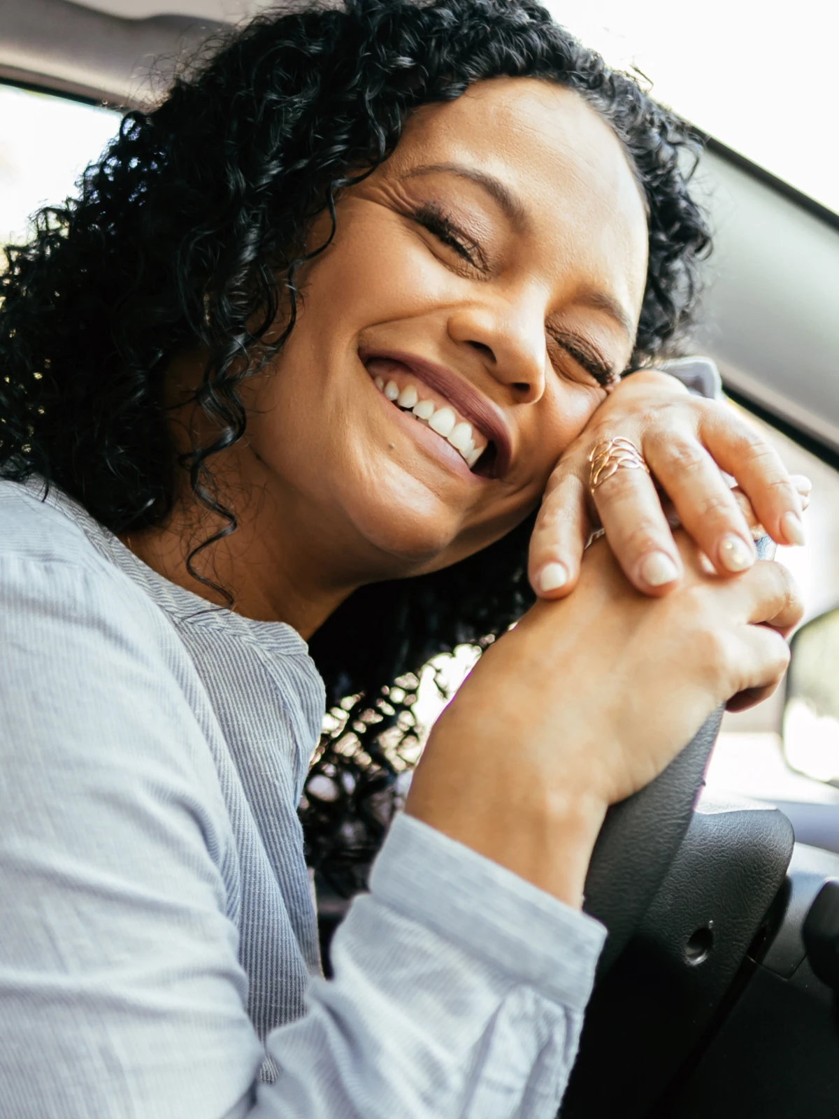 Woman laughing with her head resting on her hands on the steering wheel