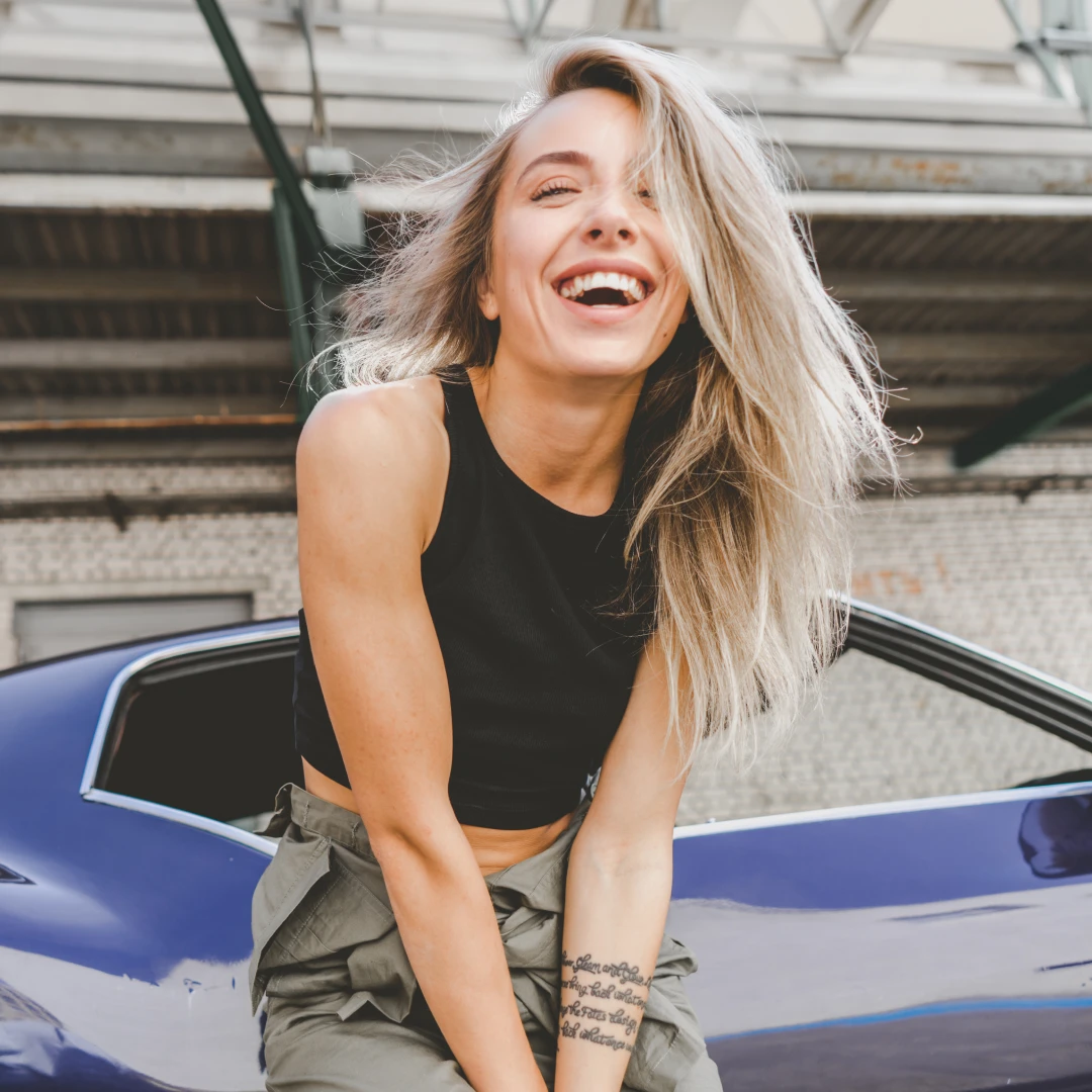 Woman laughing while sitting on a car