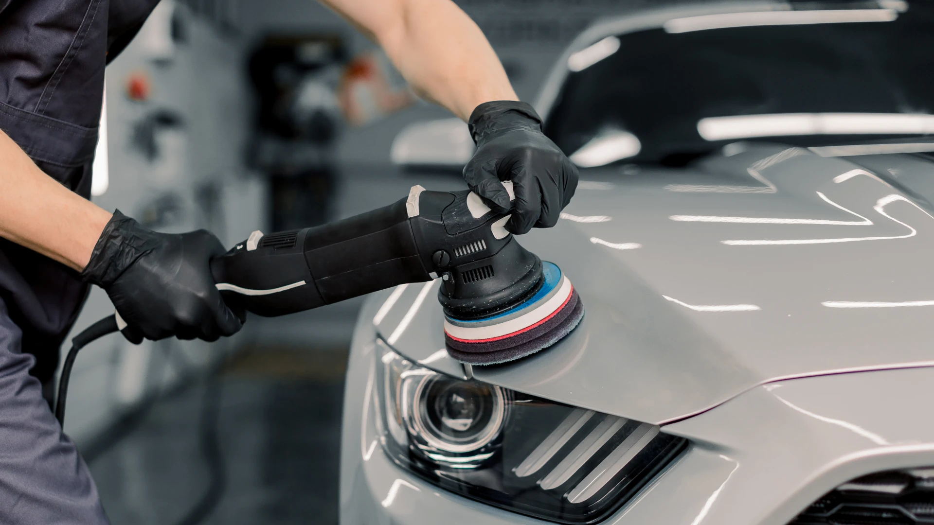 Technician using a dual-action polisher to detail the hood of a silver car